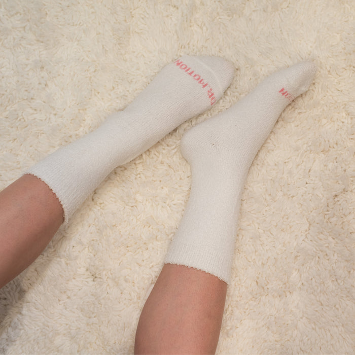 White diabetic socks with a soft texture, worn on feet resting on a fluffy surface.