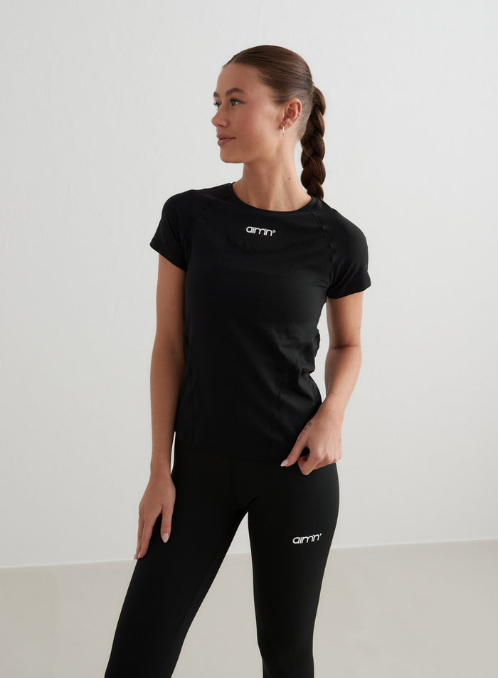 Black aim'n Soft Basic Short Sleeve workout top with a white logo, styled with matching black leggings.