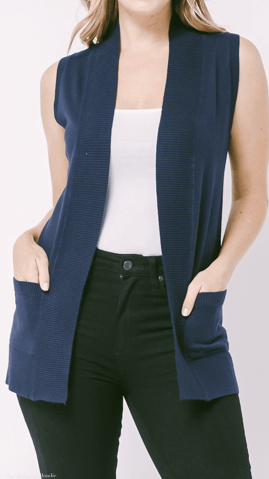 Woman wearing sleeveless navy blue open-front cardigan with pockets over white top and black pants