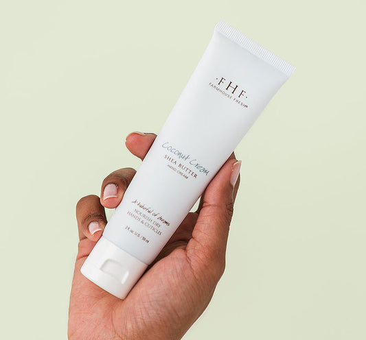 Hand holding a white tube of Coconut Cream Shea Butter Hand Cream | Farmhouse Fresh against a light background, showcasing skincare for soft and nourished hands.