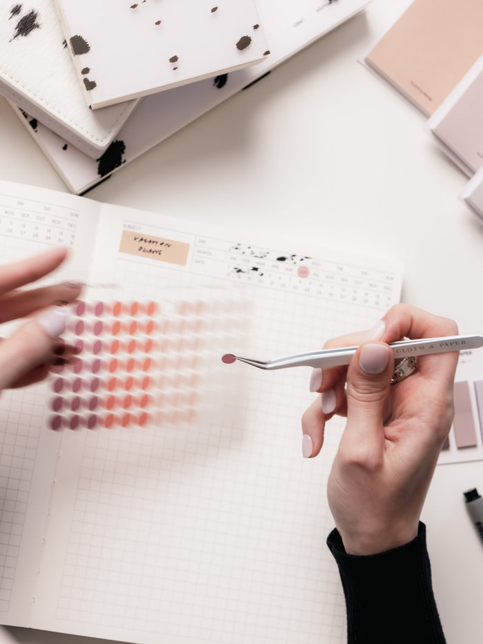 A person applying Dot Stickers | Small using tweezers to a planner