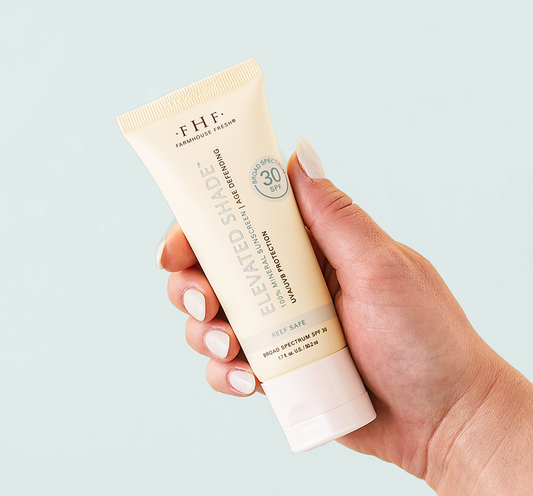 Hand holding a tube of Elevated Shade® Age-Defending 100% Mineral Sunscreen | Farmhouse Fresh with SPF 30 for skincare and sun protection.