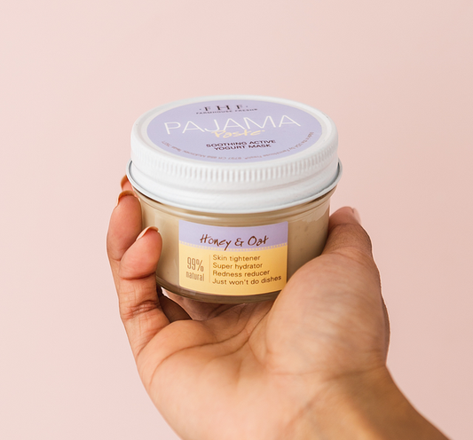 Hand holding a jar of Pajama Paste® Soothing Active Yogurt Mask | Farmhouse Fresh with label highlighting honey and oat ingredients, skin tightening, hydration, and redness reduction benefits against a soft pink background