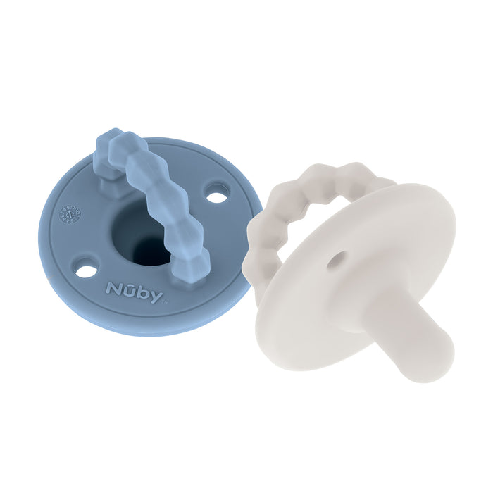 Two Nuby Silicone Softees Pacifier & Teether (2 Pack) are shown—one blue, one white—with round bases and wavy textured handles; the blue pacifier is embossed with the brand name, ideal for soothing your baby.