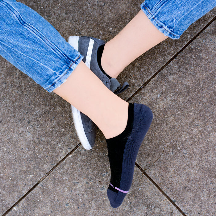 Liner compression socks in black and gray worn with casual shoes, resting on a concrete surface.