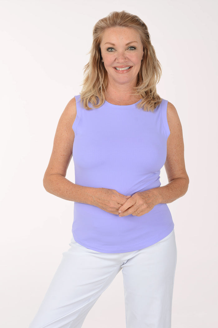 Woman wearing a light purple sleeveless top and white pants on a white background