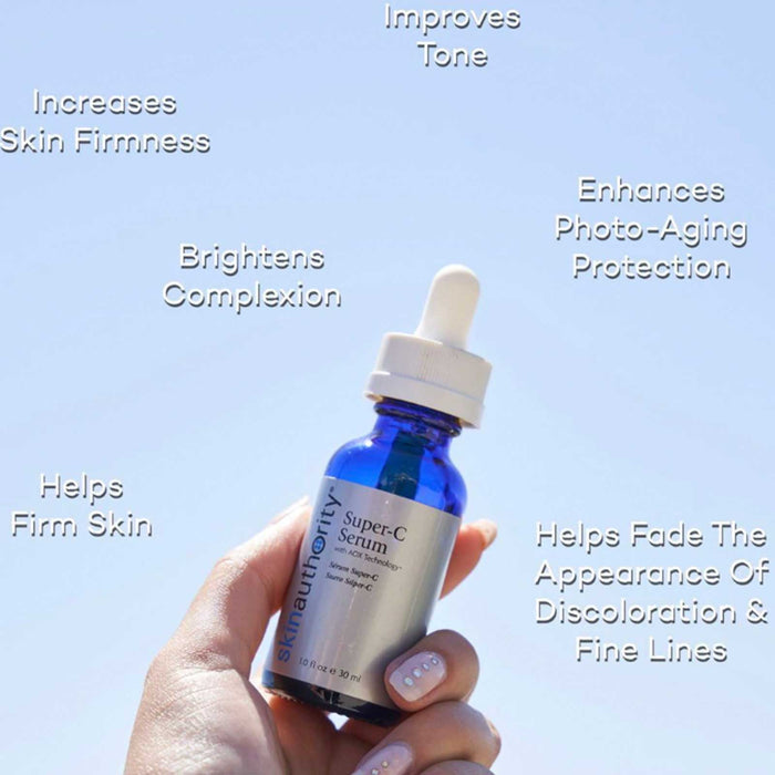 Hand holding a blue dropper bottle of Super-C Serum | Skin Authority against a clear blue sky with text highlighting benefits like improving tone, increasing skin firmness, brightening complexion, enhancing photo-aging protection, and helping fade discoloration and fine lines.