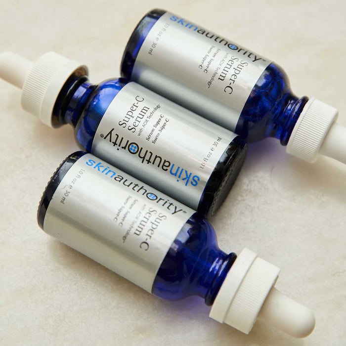 Three blue glass dropper bottles of Super-C Serum | Skin Authority with silver labels displayed on a light surface, highlighting skincare products for daily wellness.