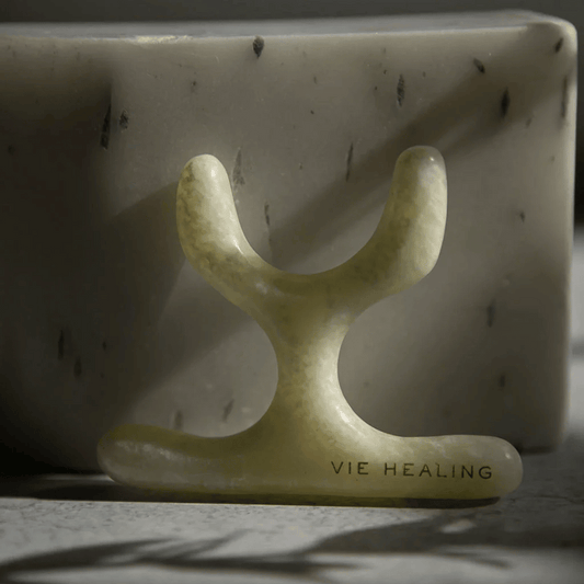 U Shape Jade Gua Sha | Vie Healing tool made of smooth green jade, designed for skincare and facial massage, placed against a textured stone background in natural light.